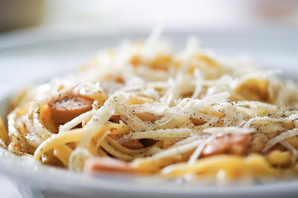 Spagetti carbonara upplagt på en tallrik. Ovanpå spagettin är det riven ost och svartpeppar.